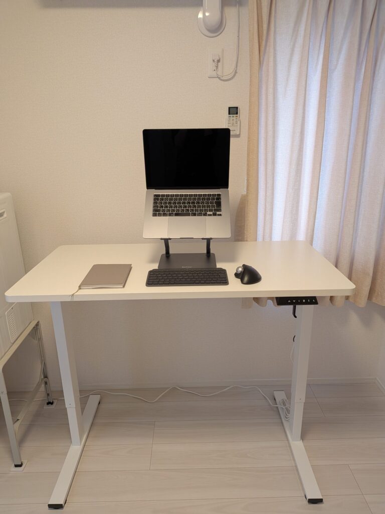 ノートパソコンスタンドとワイヤレスキーボードを配置した、ミニマルなデスク上の様子